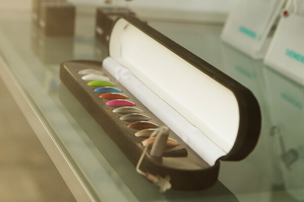 Offene Box mit bunten Hörgeräten auf einem Glastisch im Hörgerätefachgeschäft.