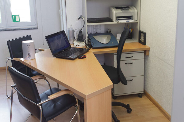 Modernes Büro mit Schreibtisch, Laptop, Drucker, Stuhl und zwei Besucherstühlen.